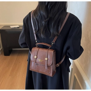Close-up of vintage brown leather backpack with gold buckles worn by a model in soft light
