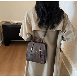 Detail of vintage dark brown square crossbody bag on model wearing a beige trench coat