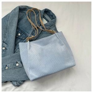 Detail of light blue tote bag with diamond quilted texture and slim brown leather straps