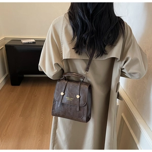 Detail of vintage brown PU leather backpack with gold accents on khaki trench coat