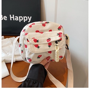 Detail of beige corduroy crossbody bag with red strawberry embroidery and woven pendant