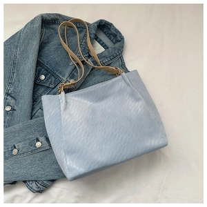 Detail of light blue woven texture tote bag with khaki straps on denim background