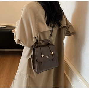 Detail view of a vintage dark brown PU leather backpack on a beige trench coat