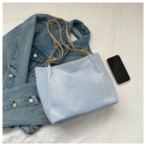 Close-up of light blue quilted tote bag on white fabric with denim jacket and smartphone