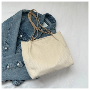 Detail of cream waffle texture tote bag with khaki straps and gold hardware on white cloth