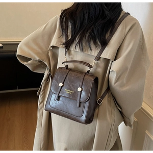 Detail of vintage dark brown PU leather backpack with gold lettering on beige trench coat