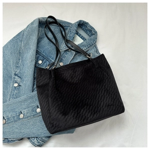 Detail of black tote bag featuring geometric quilted texture and slim shoulder straps