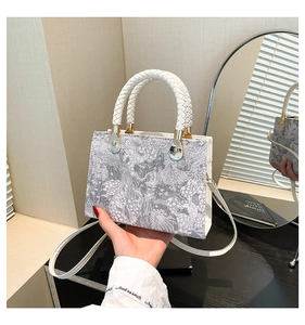 Detail of grey floral embroidery texture on handbag with white woven handle and leather strap