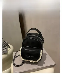 Detail of mini black backpack with white lace trim, bow, and chain straps on shelf