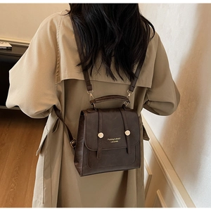Deep brown vintage PU leather backpack with gold buckle details worn over a beige coat