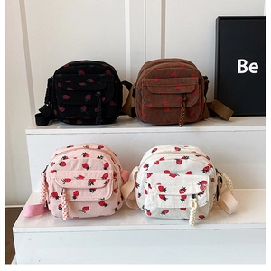 Detail of four colorful corduroy crossbody bags with strawberry prints in a tiered display