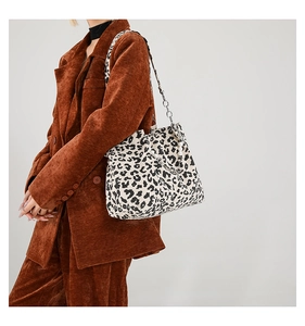 Leopard print tote bag with pearl charms and silver chain shown on a brown corduroy suit