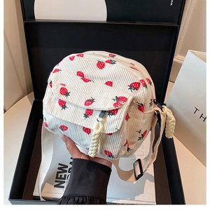 Detail of corduroy strawberry crossbody bag with decorative braid zipper pull and strap