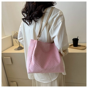 Rear view of a model wearing a pink woven tote bag with slim brown shoulder straps