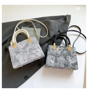 Detail of woven floral patterns and gold hardware on boxy luxury crossbody handbag