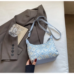 Detail of light blue crossbody bag with geometric embroidery on white linen bedding
