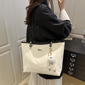 Large cream tote bag with black trim and plush monster charm shown on shoulder