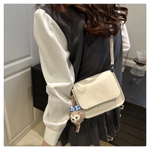Sac bandoulière beige chic avec motifs animaliers et breloque porté par un mannequin
