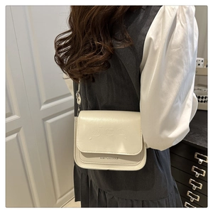 Détail d'un sac bandoulière en cuir blanc cassé avec gaufrage dessin animé et logo