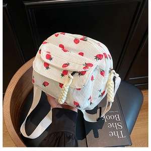 Detail of white corduroy crossbody bag with red strawberry print and cotton tassel zipper