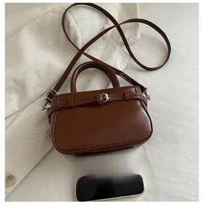 Detail of a brown leather-textured handbag with belt buckle and crossbody strap