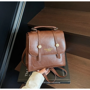 Detail of vintage brown PU leather backpack with metal buckles and handle on wooden stairs