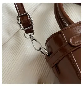 Detail of silver metallic hardware hook and adjustable strap on a brown leather handbag
