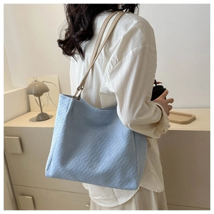 Detail of light blue tote bag with quilted texture and beige leather shoulder straps