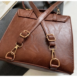 Close-up of brown leather backpack featuring gold metal hooks and adjustable straps