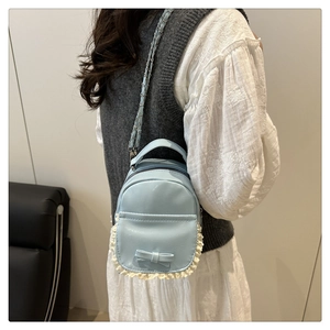 Detail eines hellblauen Mini-Rucksacks mit Schleife, Spitze und Kettenriemen