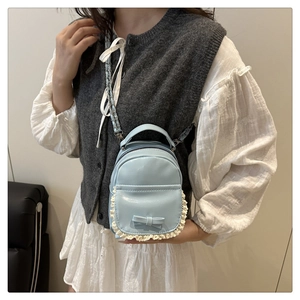 Detail der hellblauen Mini-Rucksacktasche mit weißem Spitzenbesatz und Leder-Schleife