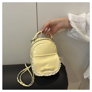 Detail eines hellgelben Mini-Rucksacks mit Spitze, weißer Schleife und Kette