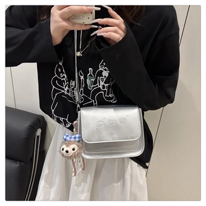 Détail du sac à bandoulière argenté métallisé avec broderie ours et porte-clés peluche
