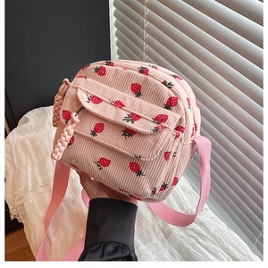 Detail of pink corduroy mini crossbody bag featuring red strawberry patterns and front pocket