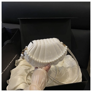 Close-up of white shell-shaped handbag featuring faux pearl decor and python texture