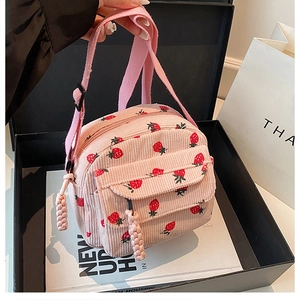 Detail of pink corduroy crossbody bag featuring red strawberry print and pocket
