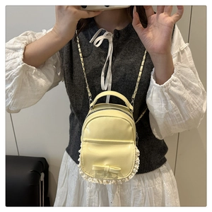 Mirror selfie showing a yellow mini backpack with lace trim and bow on a model