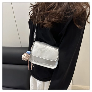 Détail d'un sac bandoulière argenté avec des reliefs d'oursons et un petit pendentif peluche