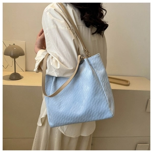 Detail of light blue textured tote bag with beige straps shown on a model