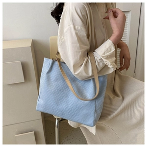 Close-up of a light blue tote bag featuring embossed woven texture and beige leather straps
