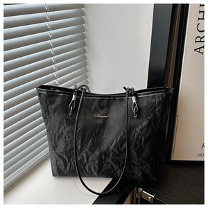 Close-up of black pleated tote bag detail showing metallic logo and wrinkled texture
