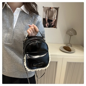 Dettaglio di mini zaino nero lucido con finiture in pizzo bianco e decorazione a fiocco