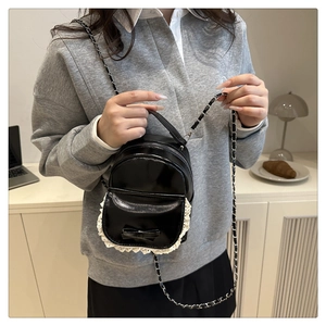 Close-up of black patent leather mini crossbody bag with white lace trim and bow detail