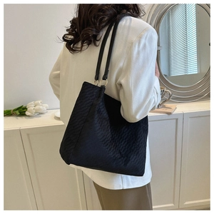 Detail of black corduroy tote bag with leather straps on a model in a minimalist setting