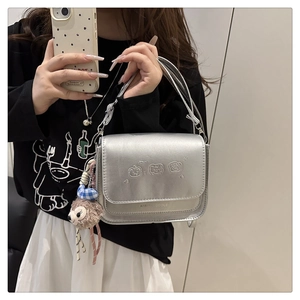 Détail d'un sac bandoulière argenté avec ours gaufrés et accessoire de sac en peluche