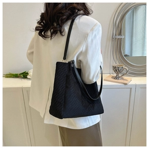 Detail of a black textured tote bag worn over the shoulder by a model in a white blazer