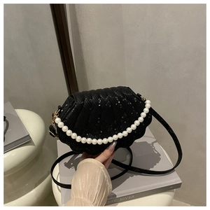 Close-up of black shell-shaped handbag featuring scale texture and decorative pearl handle