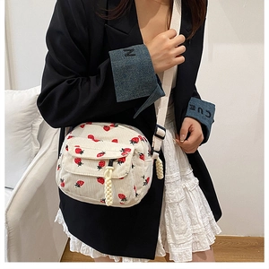 Detail of corduroy crossbody bag with strawberry print and adjustable strap worn by model