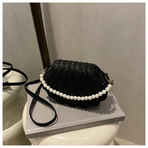 Detail of black snake-textured shell bag with white pearl chain on a grey book