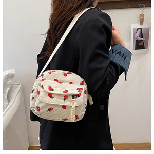 Detail of cream corduroy crossbody bag with strawberry print and woven zipper pull